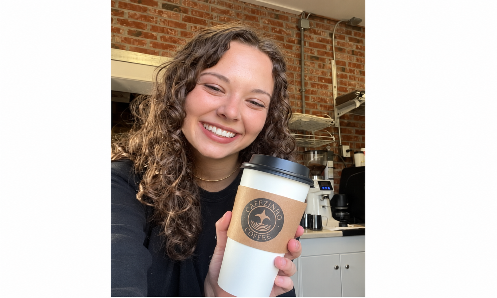 A smiling Cafezinho Coffee barista holding a branded coffee cup