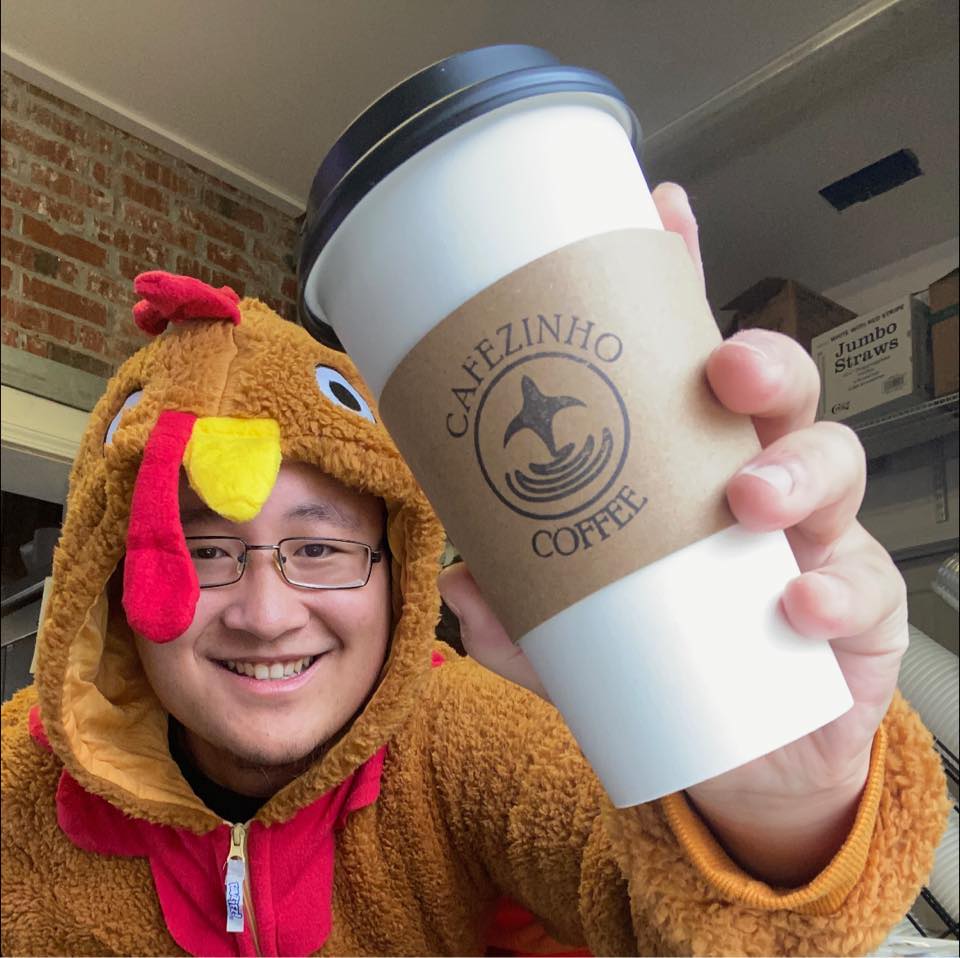 A smiling Cafezinho team member holding a branded coffee cup